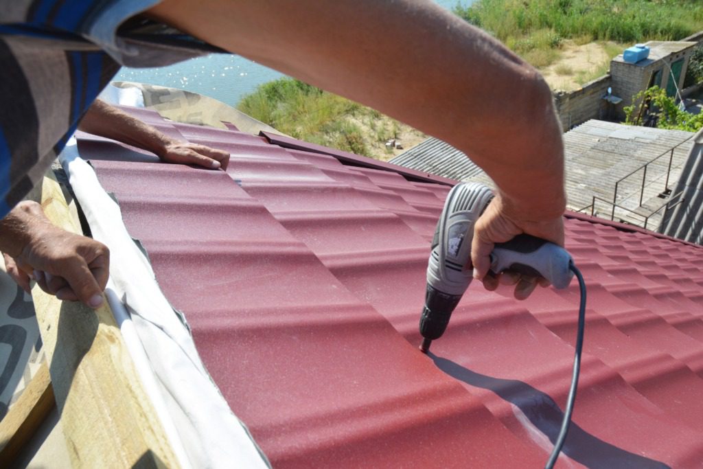 A person using a drill to install the roof of a house.