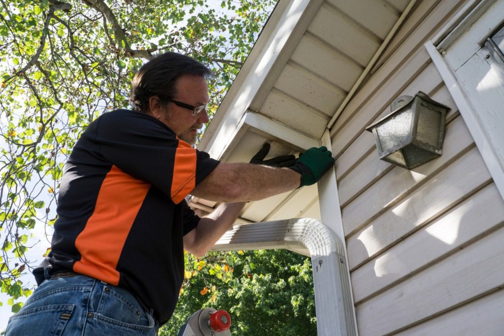 A man in an orange shirt is painting the outside of a house.
