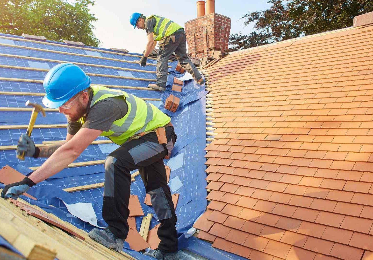 Two men working on a roof with blue shingles.