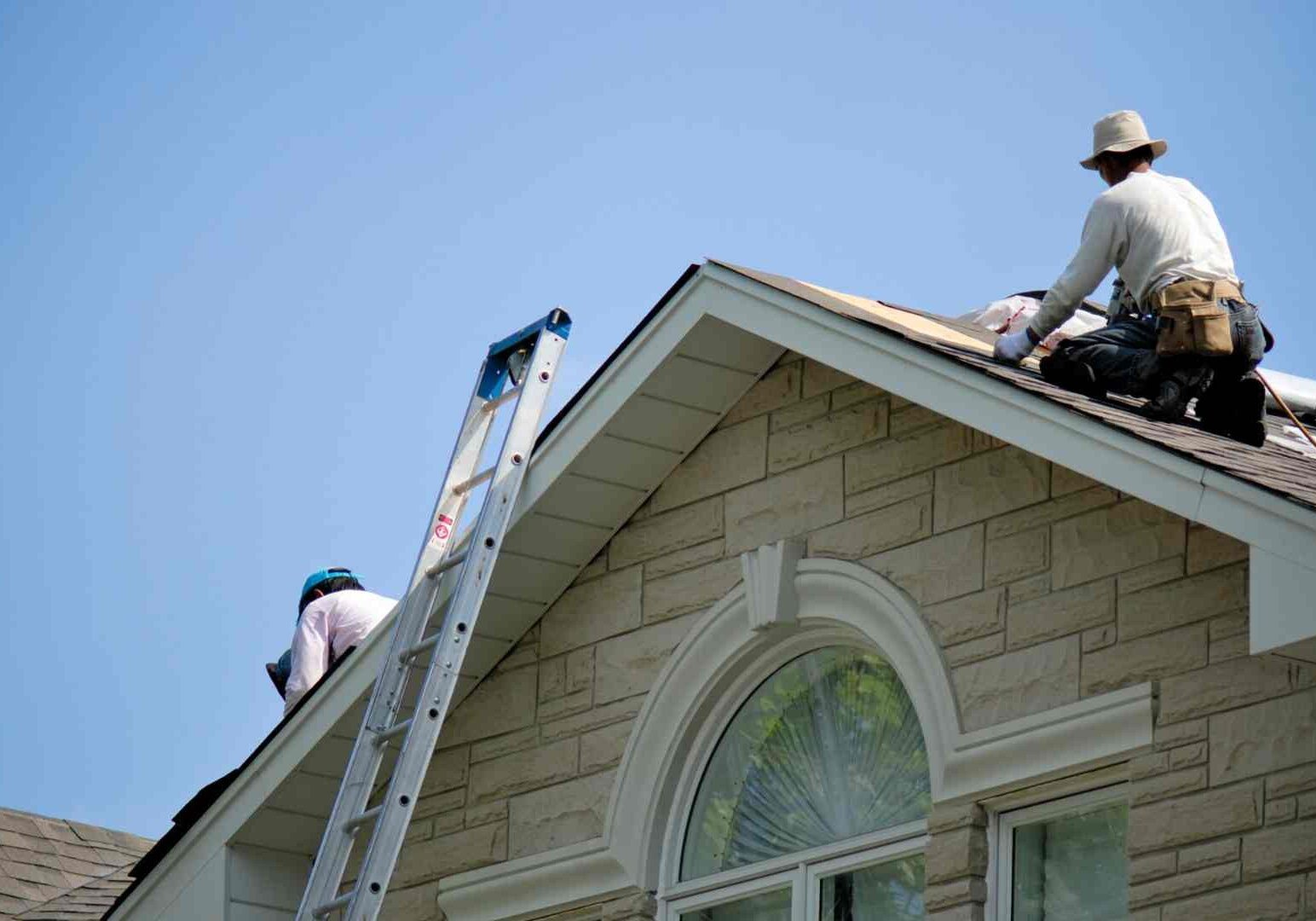 Two men on a ladder working on the roof of a house.